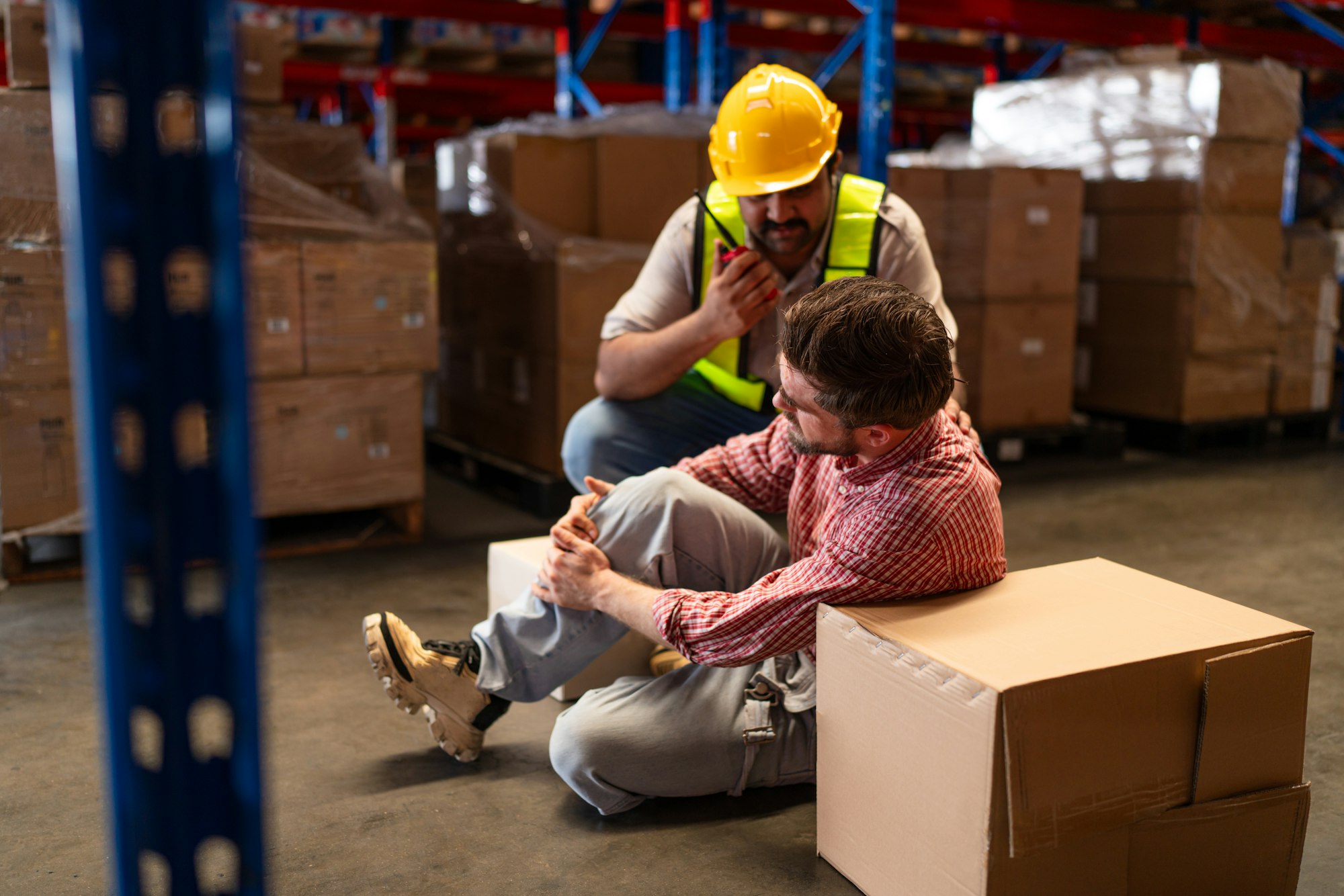 Mature foreman in workwear giving first aid to staff suffering after working injury.